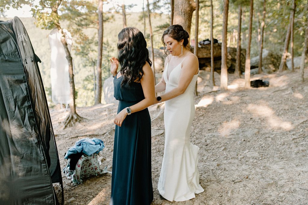 Bride helping Bridesmaid getting ready in dirt trail forest