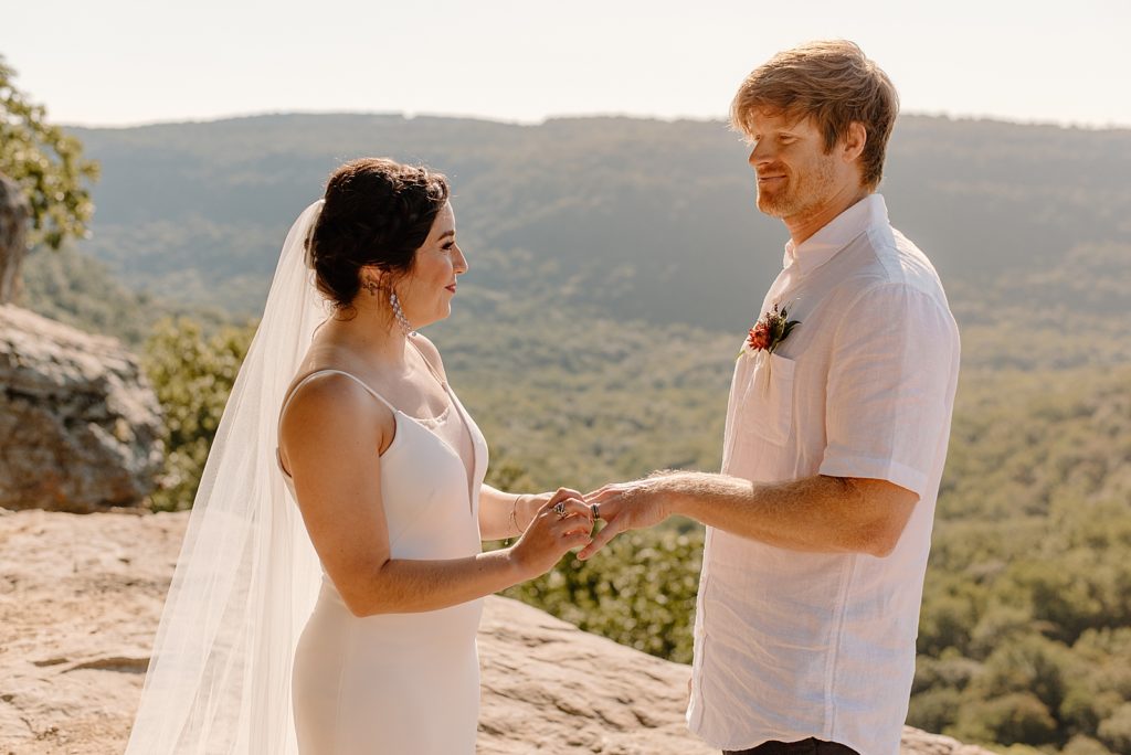 Portrait of Bride putting ring on Groom's finger by the cliff side