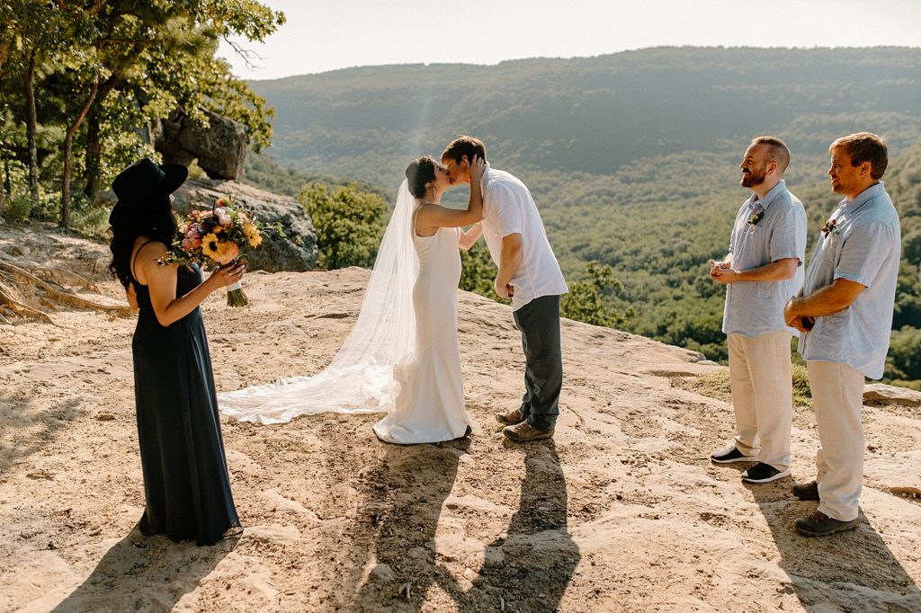 Just eloped Bride and Groom kissing by the cliff with small wedding party