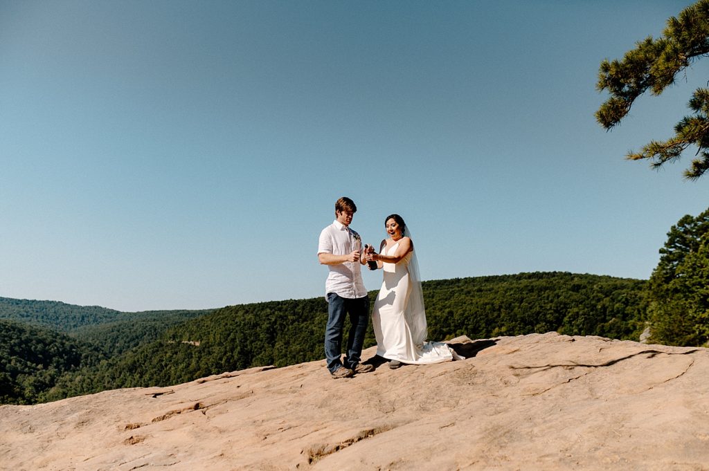 Bride and Groom on rocky cliff popping Champaign together