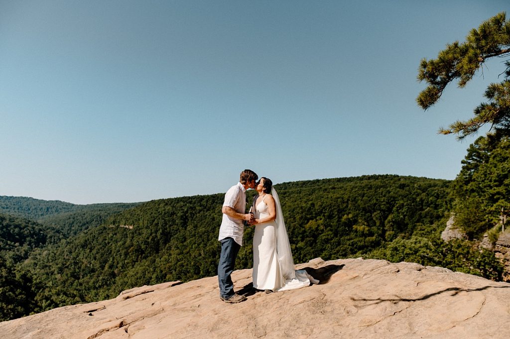 Bride and Groom on rocky cliff popping Champaign together and kissing
