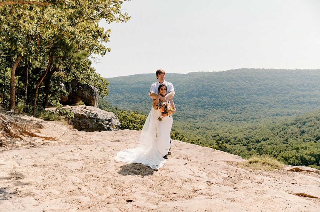 Groom holding Bride on cliff by the green forest