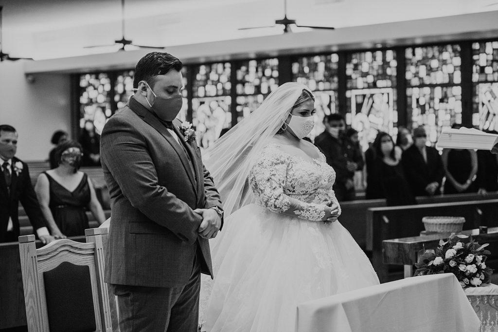 B&W Bride and Groom bowing their heads with masks on praying