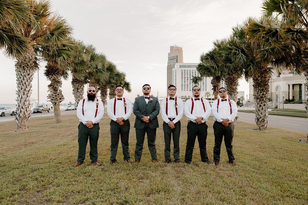 Groom and Groomsmen wearing sunglasses and red suspenders by palm trees