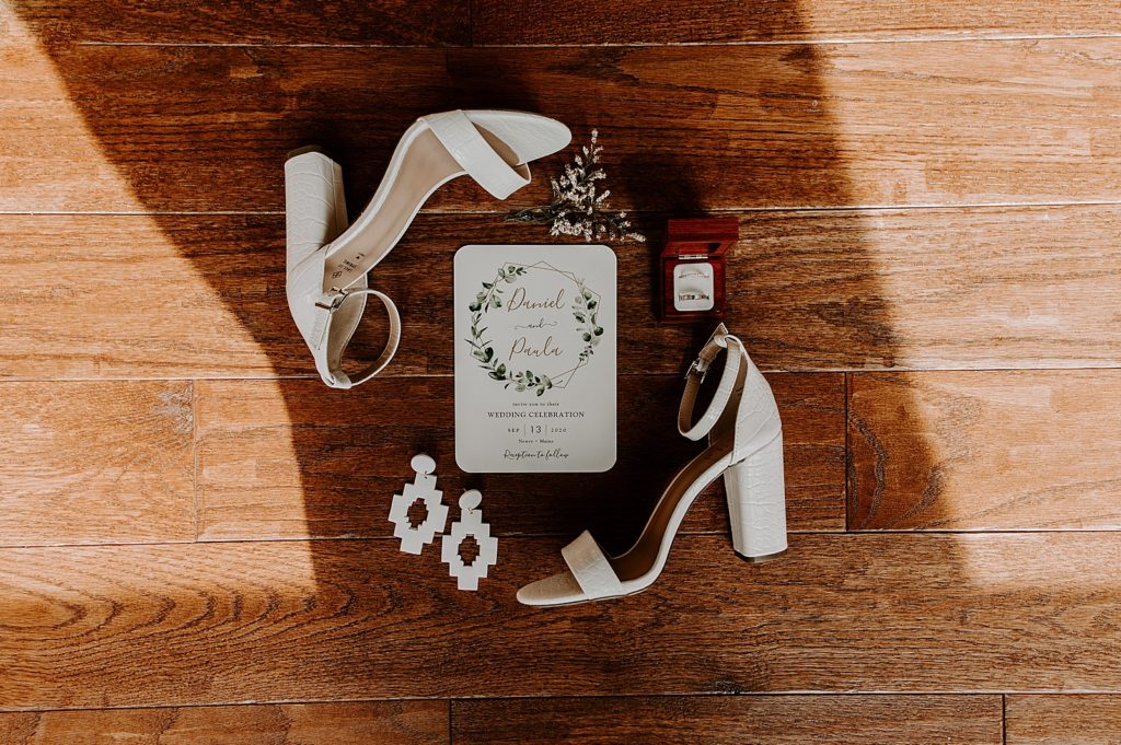 Detail shot of white heels earrings and invitation on wood floor