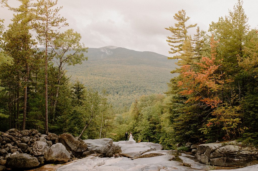 Wide shot of Bride and Groom on boulder with forest surrounding them