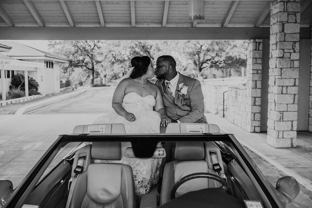 B&W Bride and Groom kissing on top of convertible vehicle 