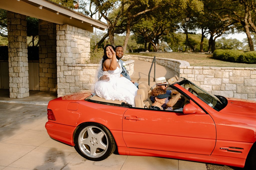 Bride and Groom riding on red convertible 