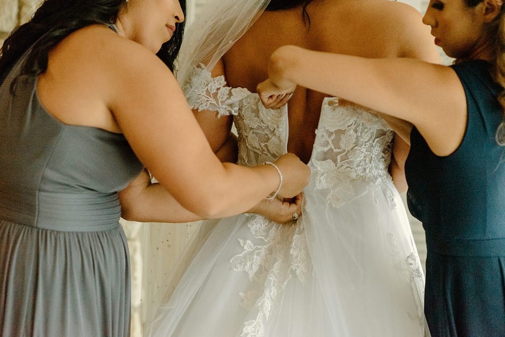 Bride getting ready with Bridesmaids helping button up Bride's dress