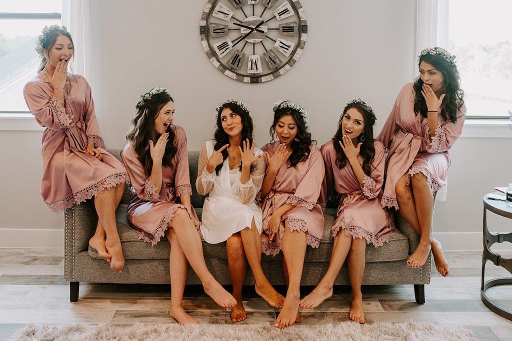 Fun Bride and Bridesmaid portrait with Bride pointing to ring on finger with Bridesmaids reacting before getting ready