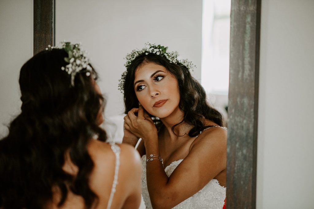 Bride looking in mirror putting on earrings