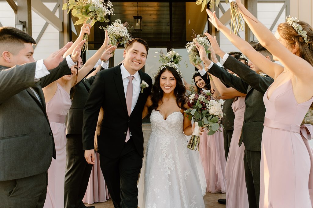 Bride and Groom walking in between wedding party with hands raised