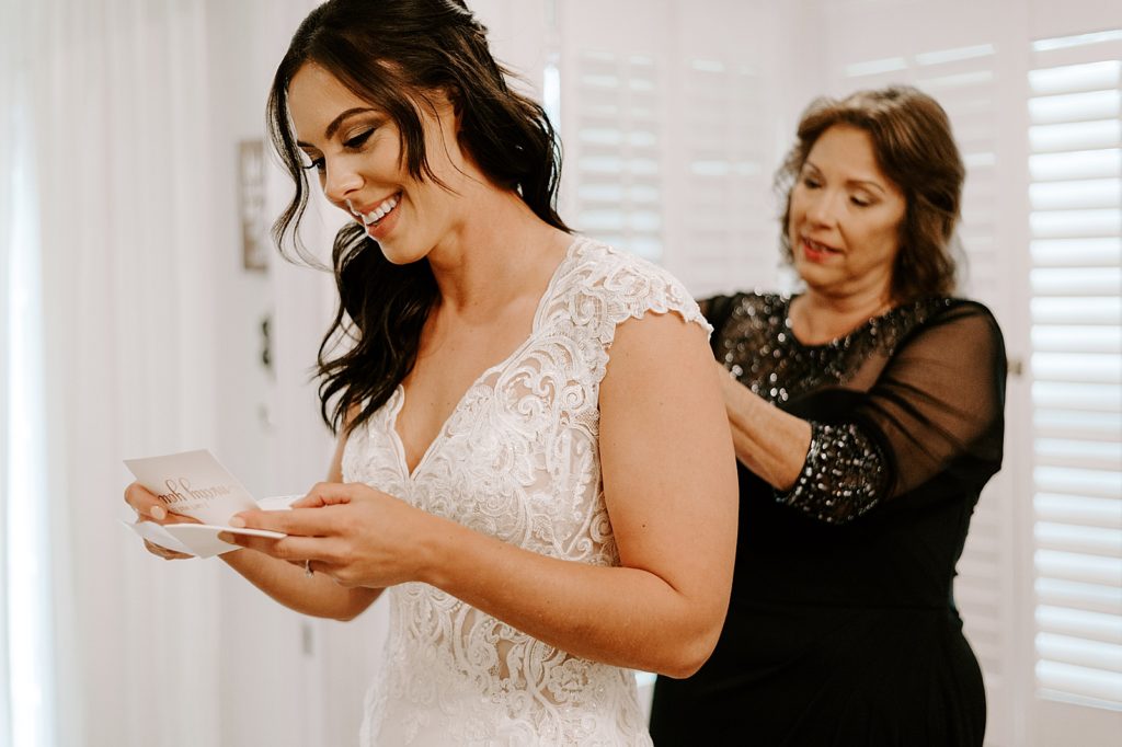 Bride reading letter while mother helps button wedding dress