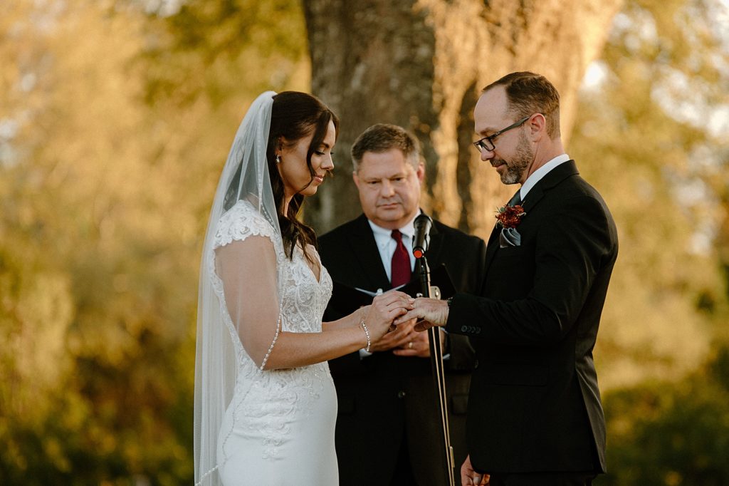 Bride putting ring on Groom during outdoor Ceremony