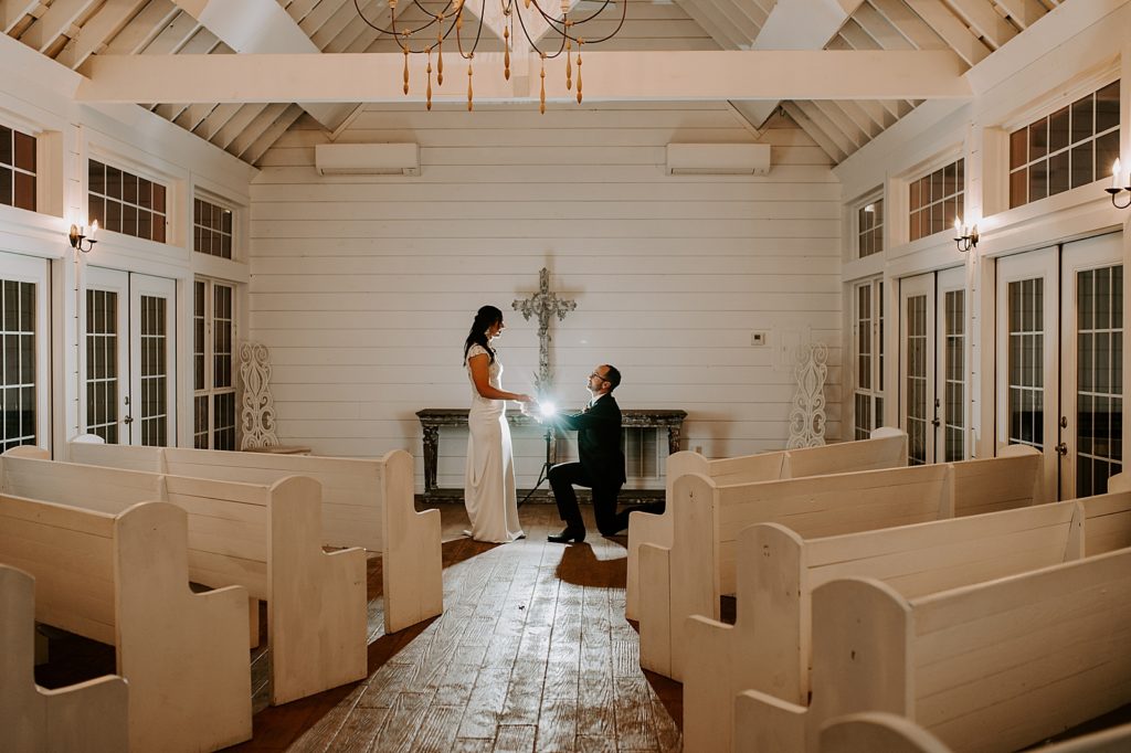 Groom on one knee in church with Bride at night