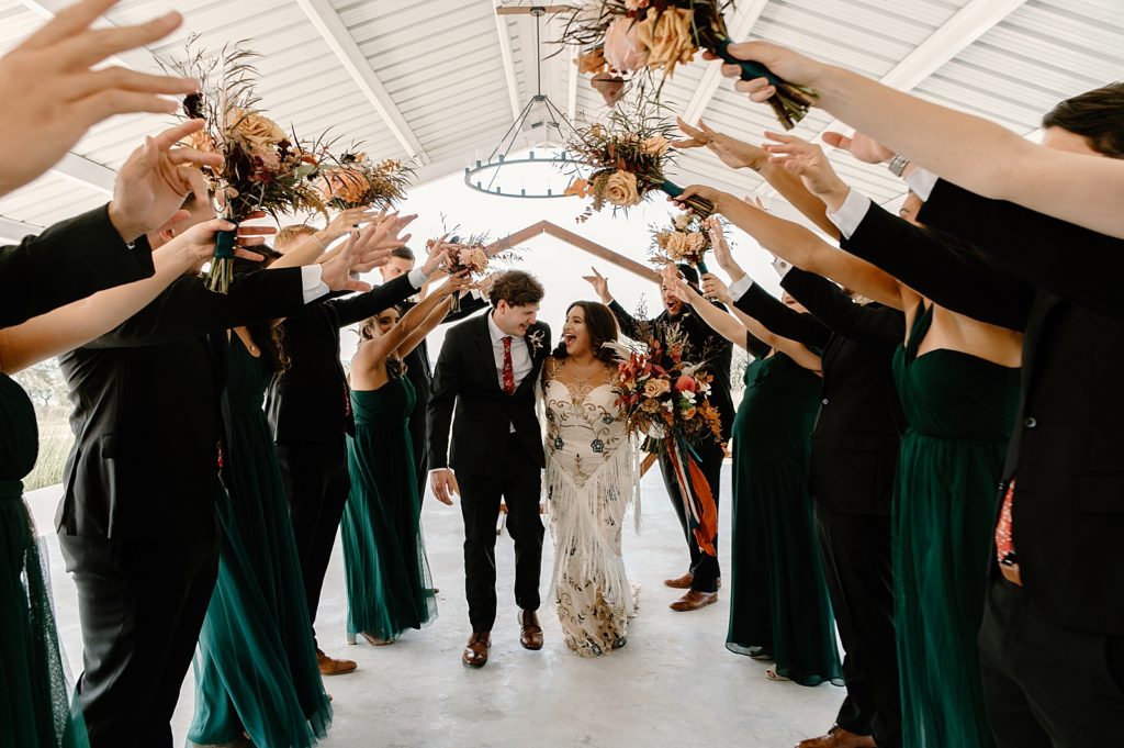 Bride and Groom walking between wedding party with hands up with bouquets in the air