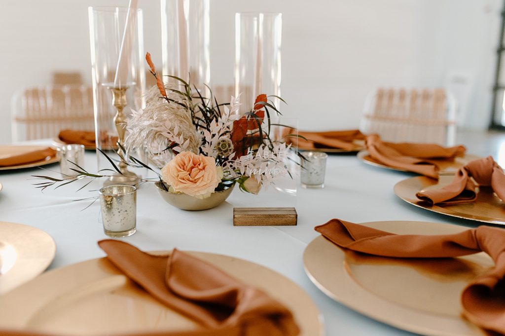 Detail shot of white table with orange accents and floral small centerpiece 
