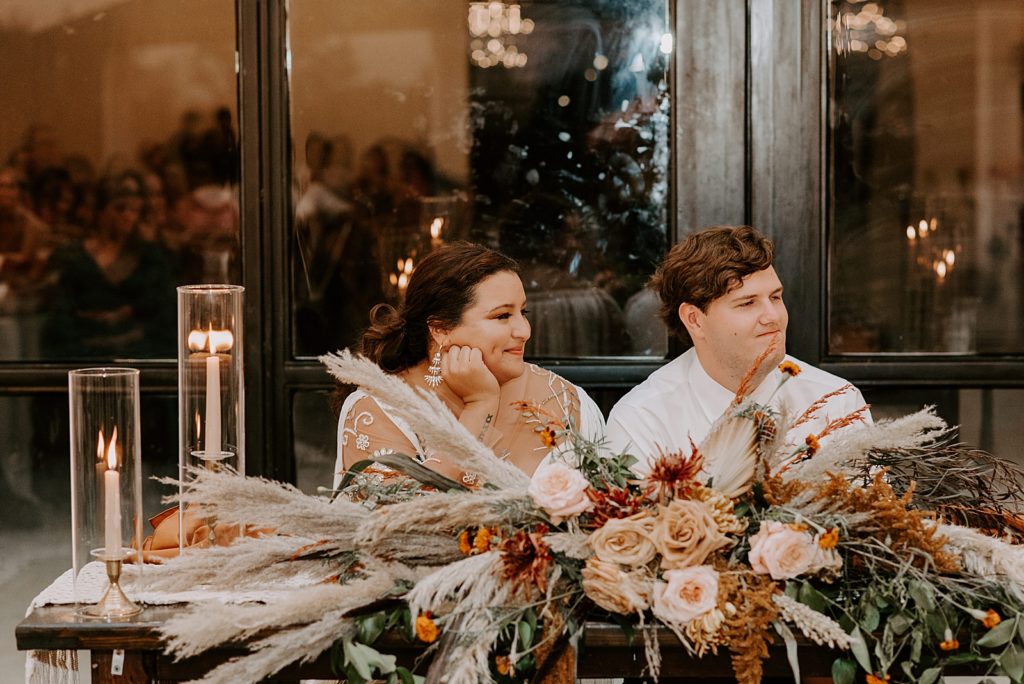 Bride and Groom listening to toast at sweetheart table with floral decor and candles