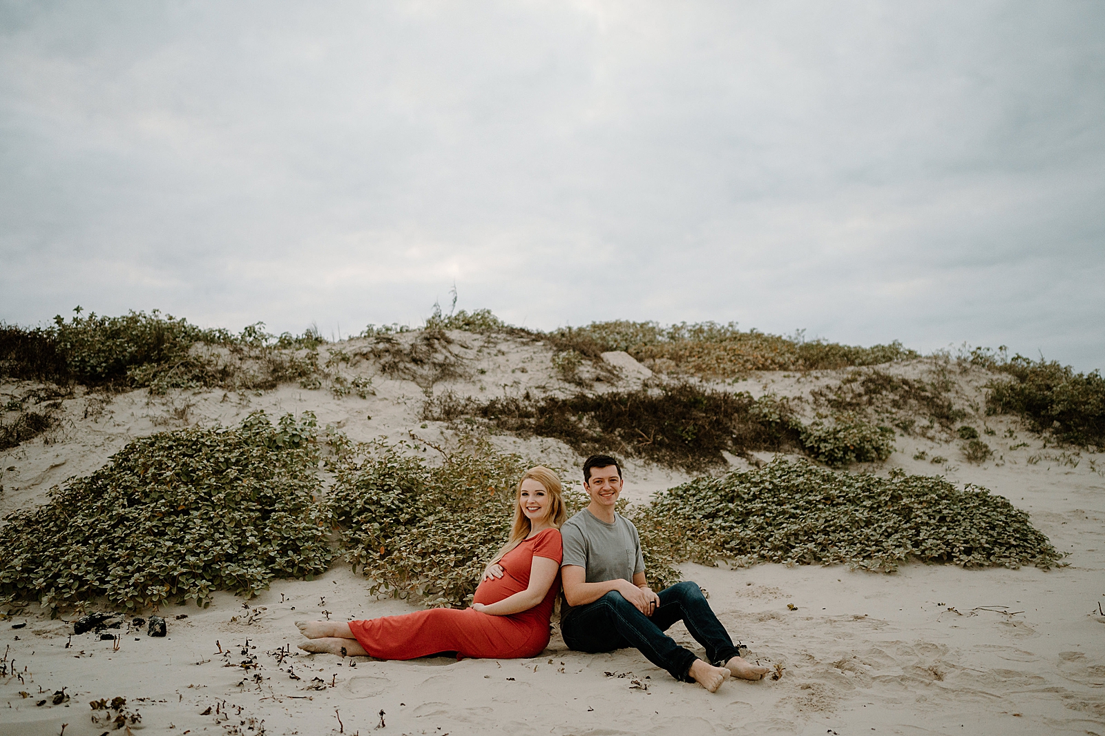 pregnant woman in red dress sitting on beach with spouse