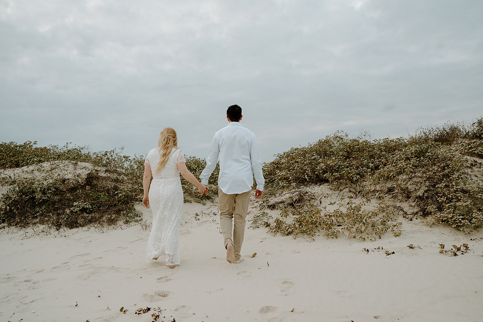 man in blue shirt holding hands with blonde woman in white dress on beach